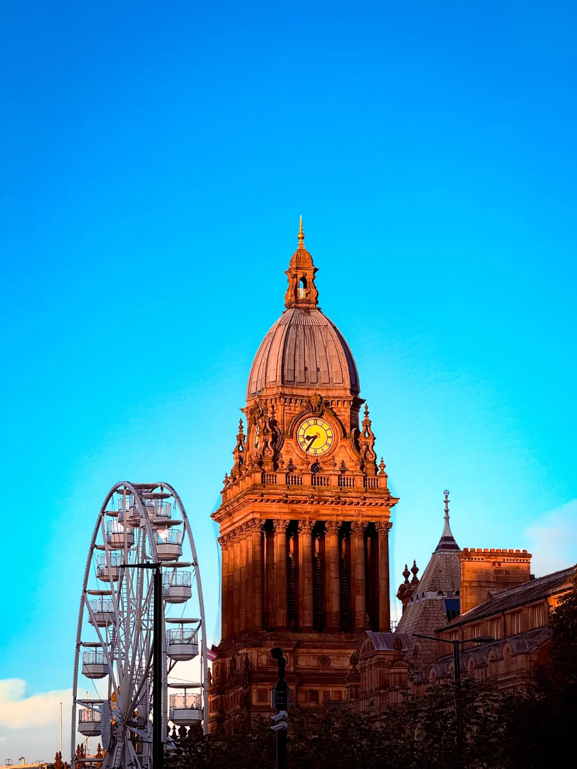 Leeds clock tower and ferris wheel against blue sky